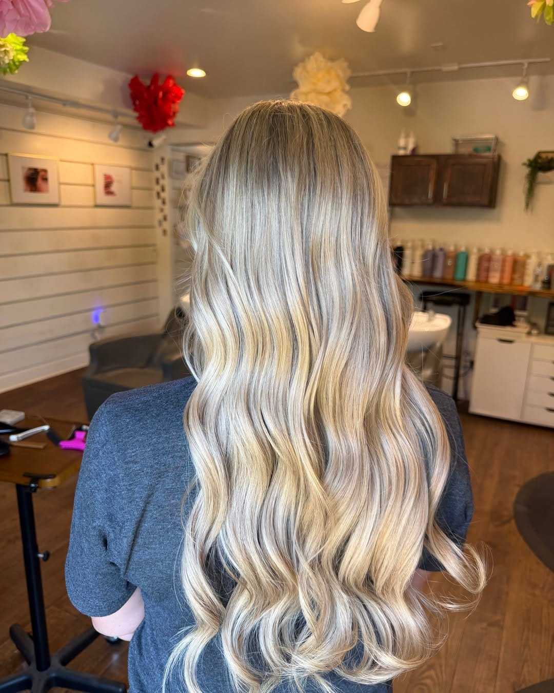 Blonde woman with long, wavy hair in a well-lit salon interior.
