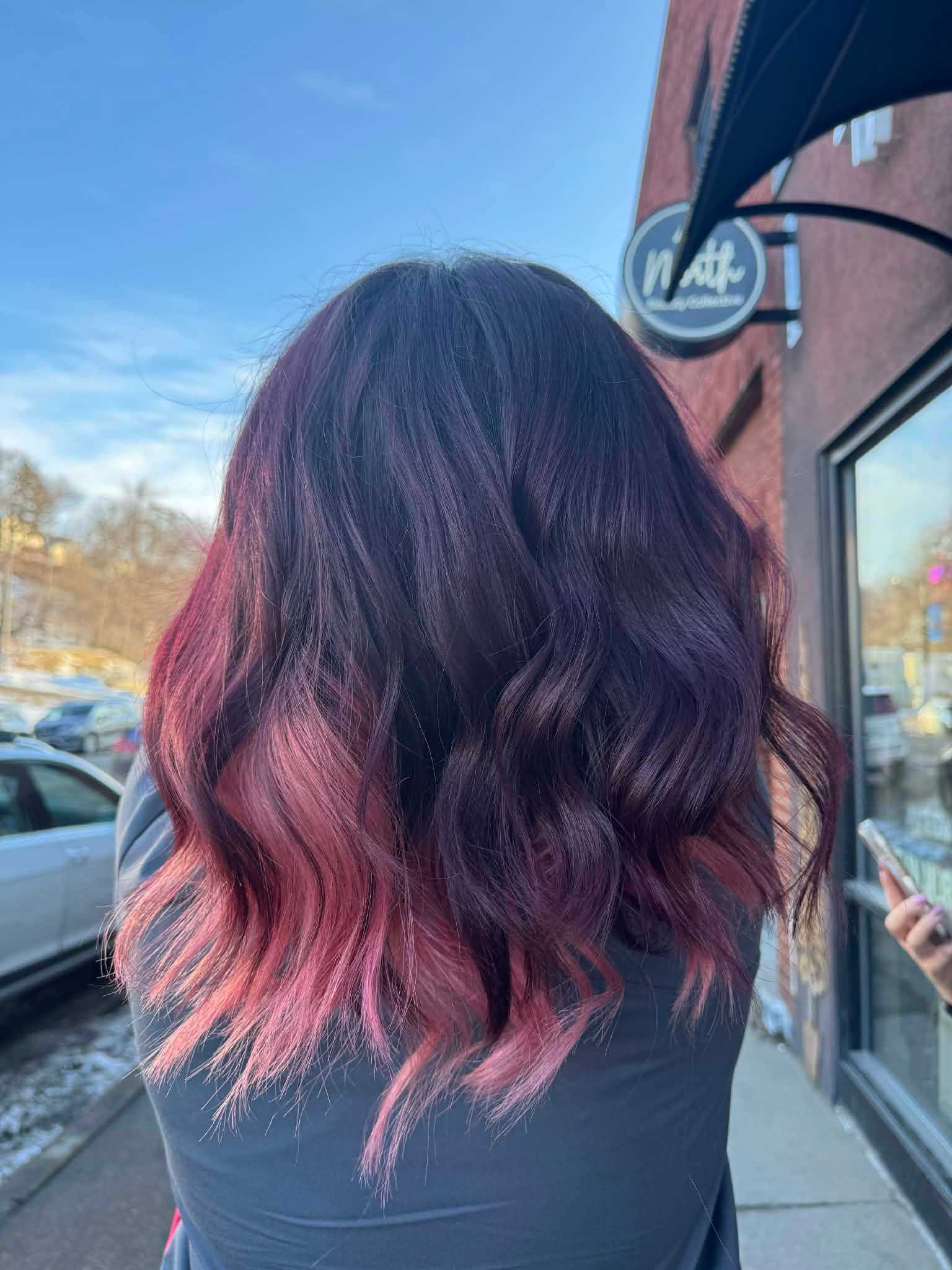 Wavy dark purple hair with pink tips, outdoors near a sidewalk and storefront.